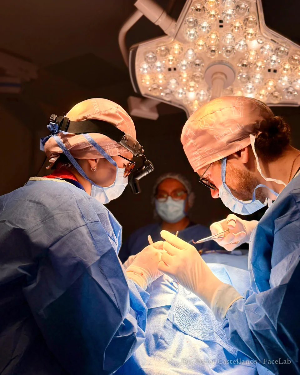 El Dr. Javier Castellanos operando bajo la lámpara quirúrgica junto a una colega, ambos con gorro FaceLab